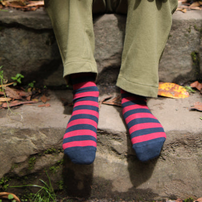 Child wearing green pants and pink and blue striped socks sitting on a stone surface.