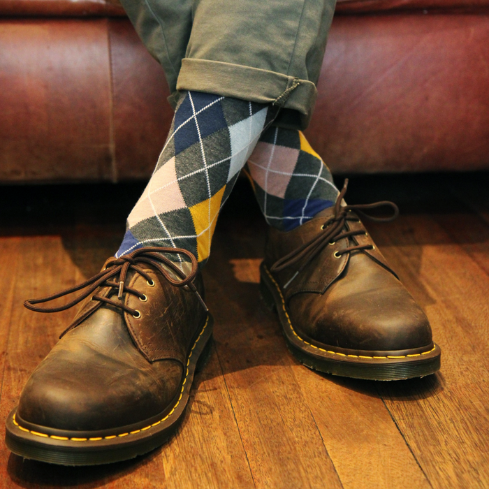 Person wearing brown leather shoes and patterned argyle socks on a wooden floor.