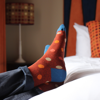 Colorful polka dot socks being worn on a bed with a blurred background