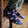 Navy blue socks with a Corgi dog pattern worn by a person on a wooden floor.