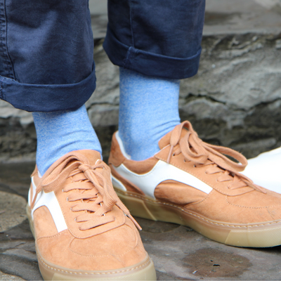 Brown sneakers with white accents worn with blue jeans and light blue socks on a stone surface.