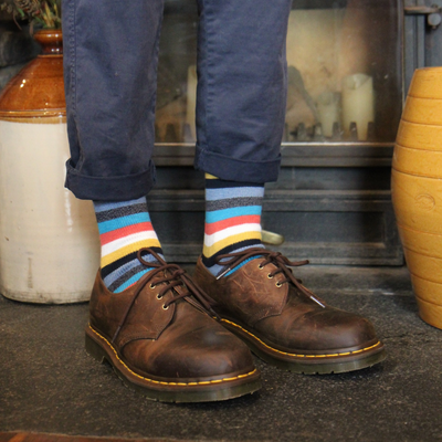 Person wearing brown leather shoes and colourful striped socks standing on a stone floor.