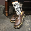 Brown leather shoes with modern floral pattern socks on a dark floor.