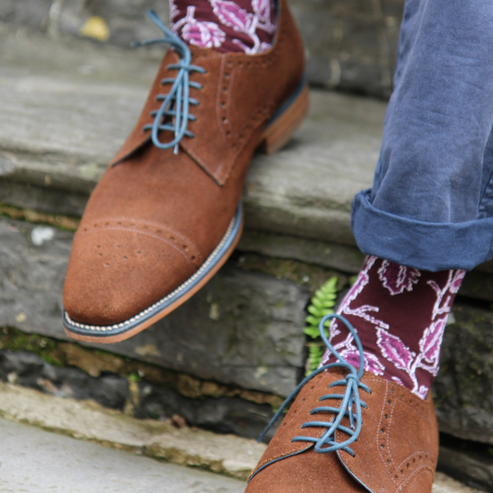 Brown leather shoes with blue laces worn with patterned socks on a stone step.