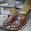 Brown leather shoes worn with green wool socks on a stone step.