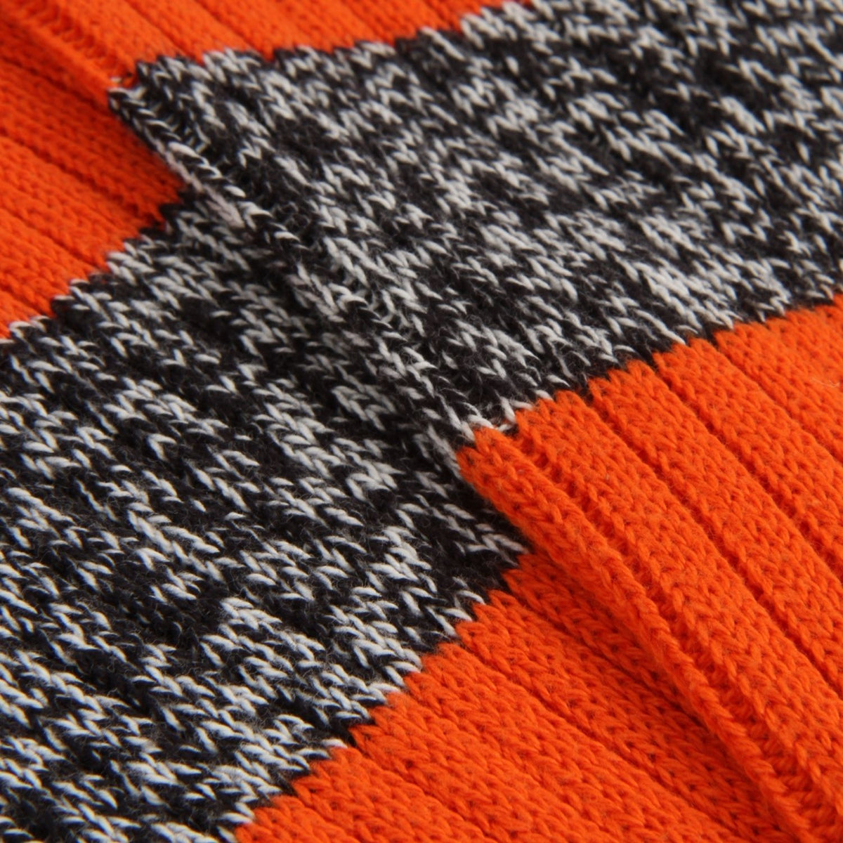 Close-up of a knit fabric with alternating sections of bright orange ribbed knit and a black-and-white heathered textured band.