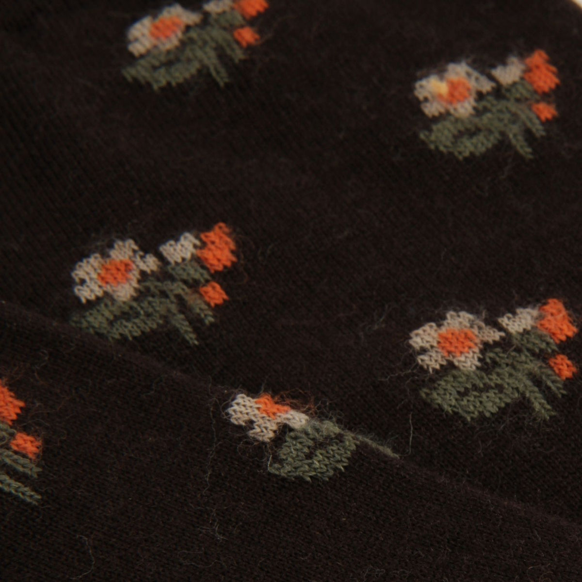 Close-up of a dark brown knit fabric with a repeating embroidered floral pattern in orange, cream, and green.