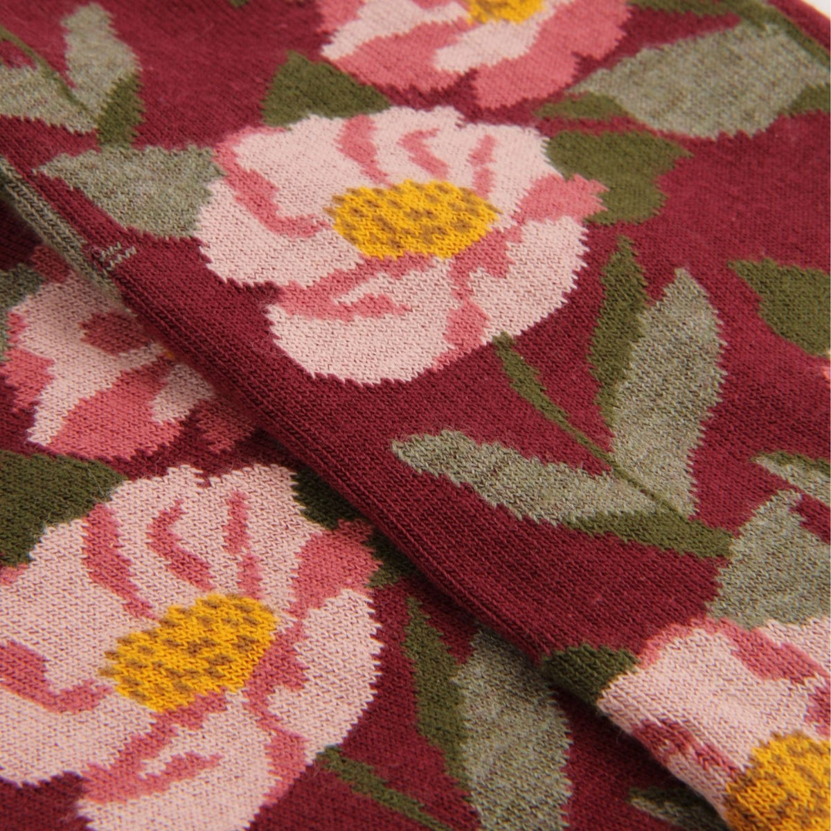 Close-up of a knitted fabric with a floral pattern featuring pink and white flowers with yellow centers and green leaves on a deep burgundy background.