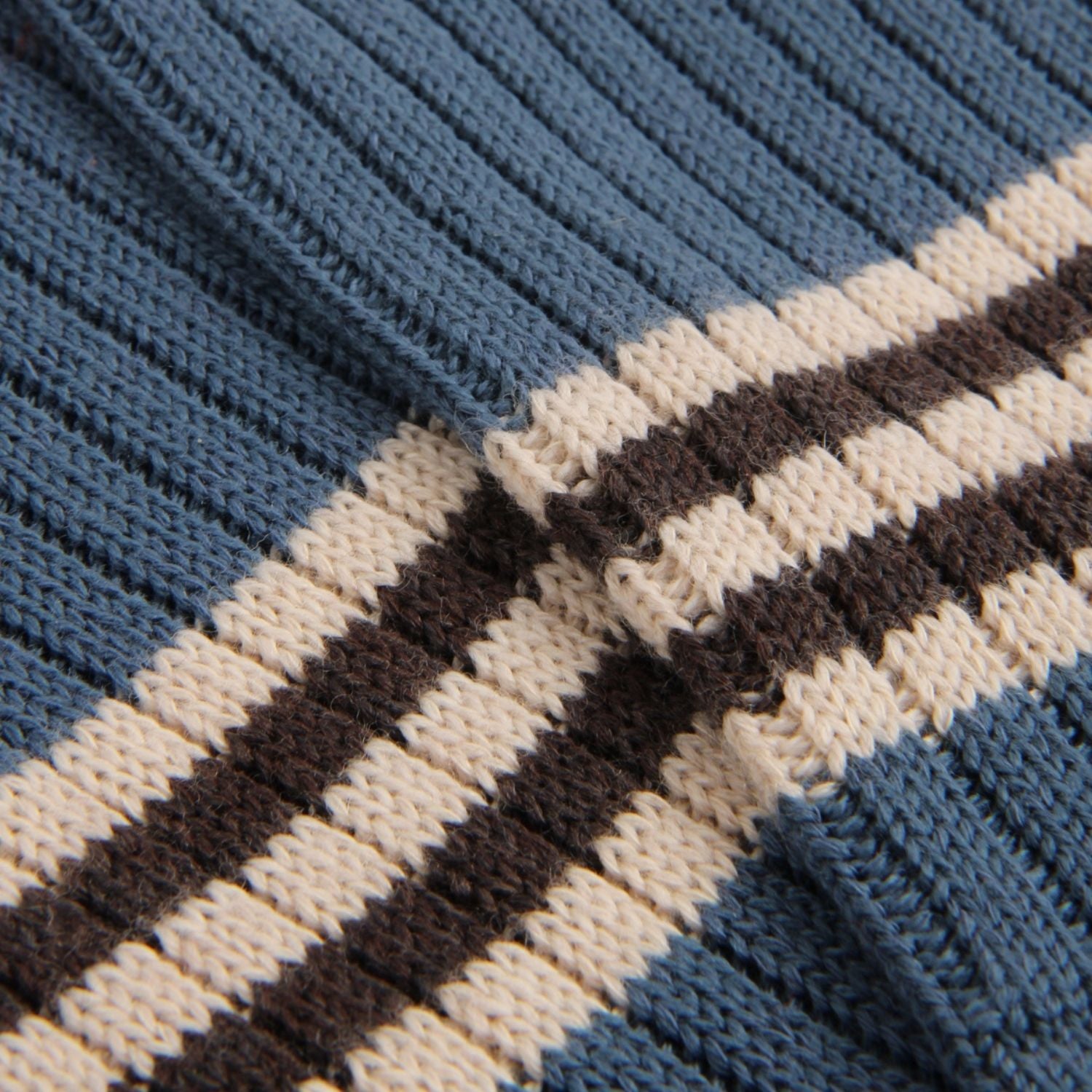 Close-up of a ribbed knit fabric with horizontal stripes in cream and dark brown over a muted blue base.