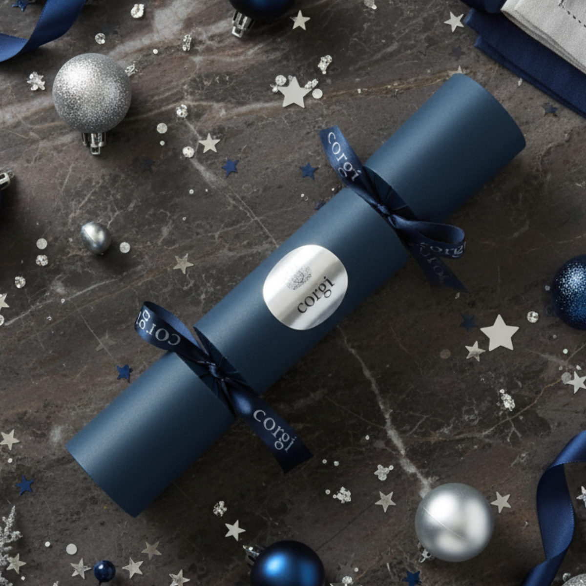 Blue Christmas cracker with 'Corgi' branding on a dark surface with festive decorations.