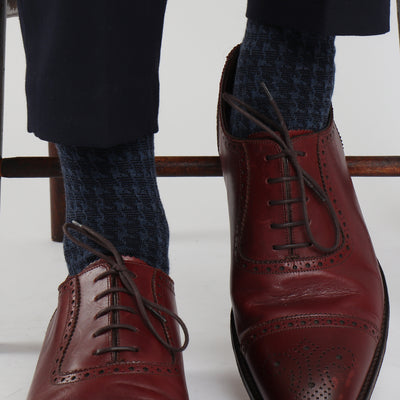 A pair of men's formal houndstooth merino wool socks in blue, showing the pattern and texture, worn with brown leather shoes.