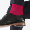 A man's leg wearing a pink ribbed sock, paired with a dark suit and a black shoe.