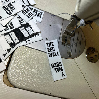 Fabric tags with text 'THE RED WALL' on a sewing machine