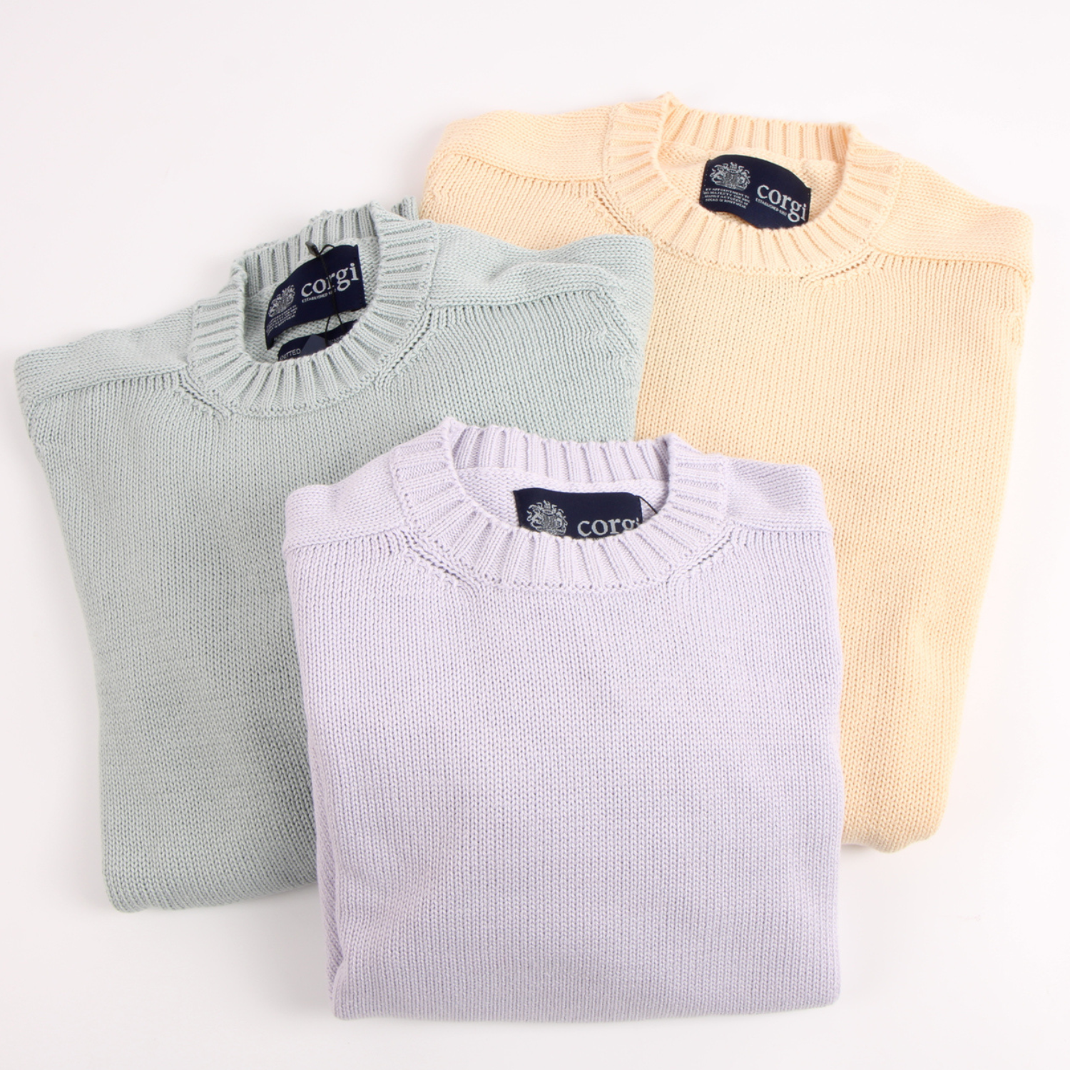 Three folded sweaters in pastel colours with 'corgi' branding on a white background