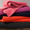 Stack of colourful throws including pink, purple, red, and black on a wooden surface.