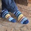Multi coloured striped socks in tones of blue with a flash of ochre worn on a wooden floor