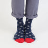 Navy socks with white snowflake patterns and red toes worn with rolled-up gray pants on a light gray background