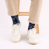 Person wearing navy leaf patterned socks with white sneakers on a light background
