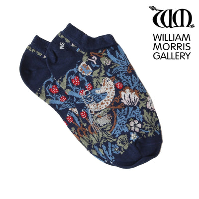 A pair of blue trainer socks with a floral pattern, featuring the 'Strawberry Thief' design by William Morris, worn on someone's feet.