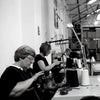 Two women working at a knitting machine in a factory setting.