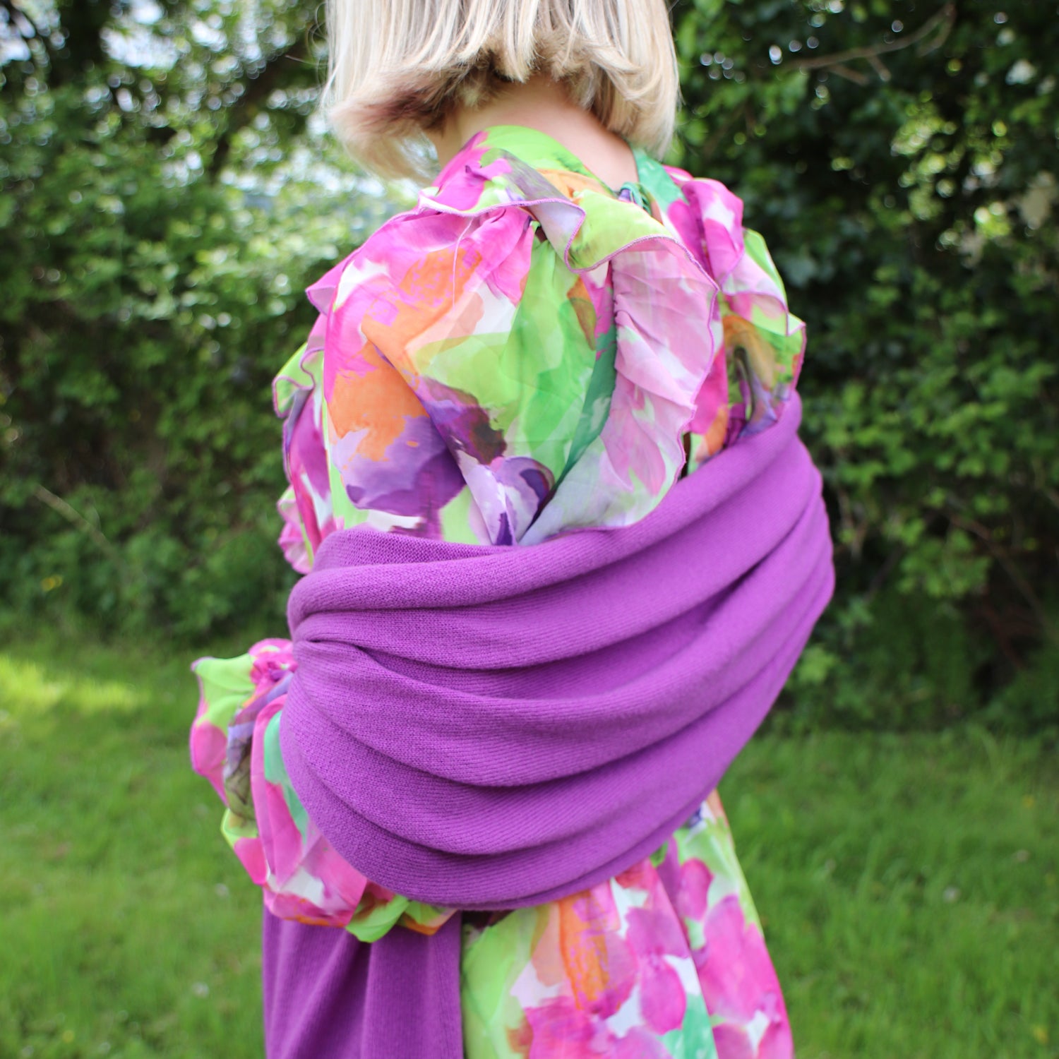 woman wearing a colorful floral-patterned dress with a purple base in an outdoor setting.