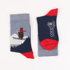 A pair of children's socks with a skiing bear design, featuring a blue colour scheme, red heel, and the brand name 'Corgi' on the foot.